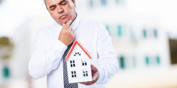 homem segurando miniatura de casa em um Feirão de imóveis.